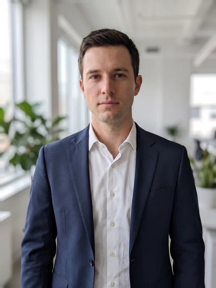 Business headshot in a navy suit against a bright blurred office