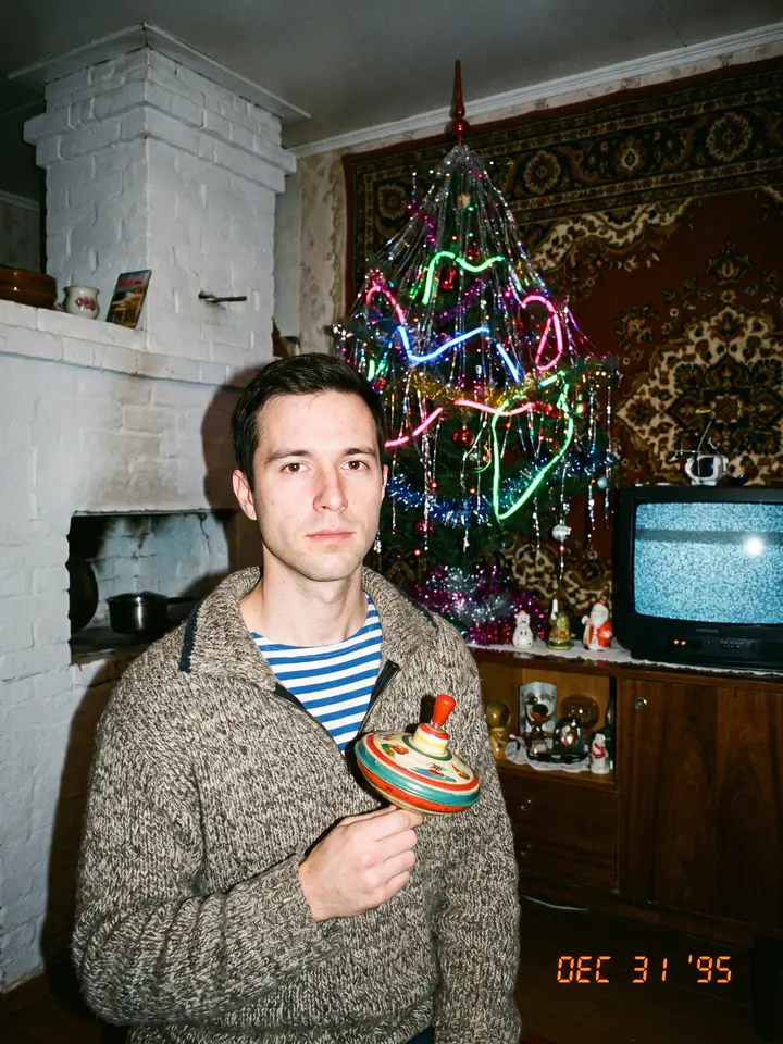 1990s flash snapshot of a man in a village room with a carpet on the wall