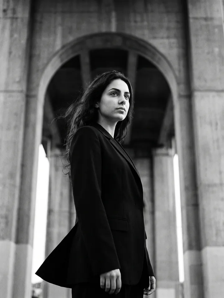 Black-and-white fashion shot in a black blazer by a concrete arch